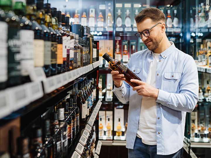 Two shelves full of whisky bottles on each side of the image and a display of lit cabinets with whisky bottles in the background.